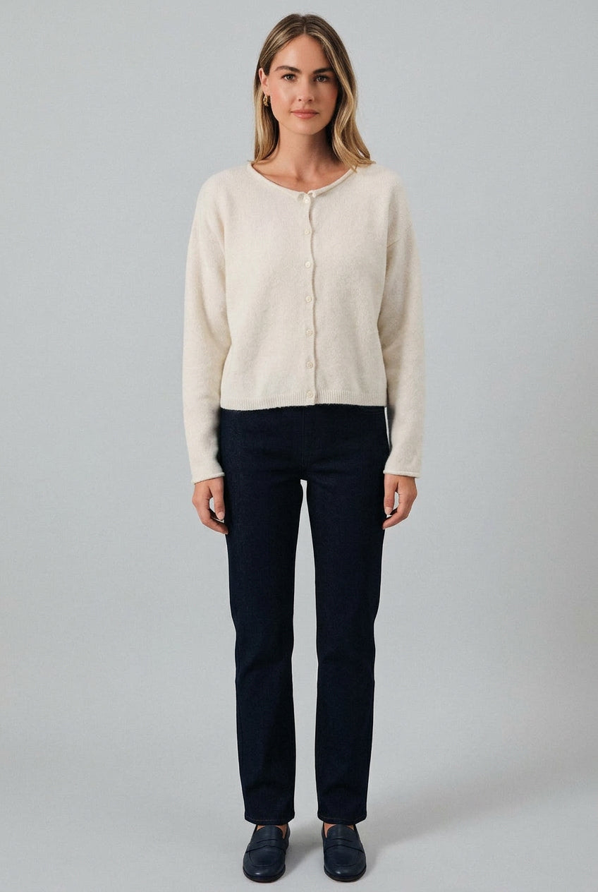 Woman wearing a cream cardigan over a black top and shorts on a gray background