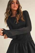 Woman wearing a black long sleeve flare dress on a beige background