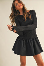 Woman wearing a black long sleeve flare dress on a beige background