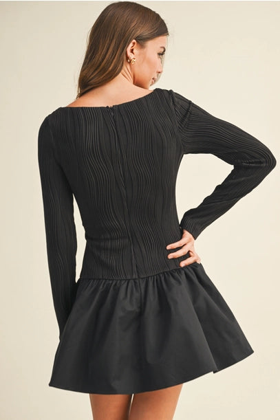 Back view of woman wearing a black long sleeve flare dress on a beige background