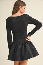 Back view of woman wearing a black long sleeve flare dress on a beige background