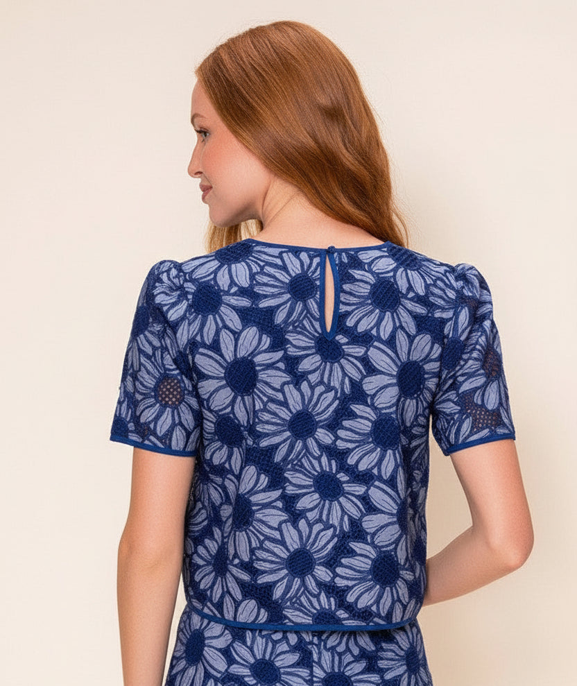 Back view of a woman wearing a blue floral embroidered top against a beige background