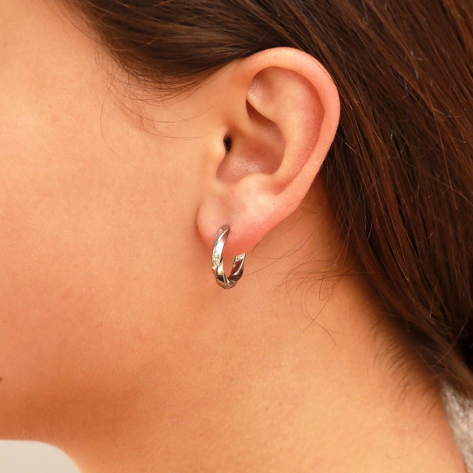 Woman wearing silver twisted huggie hoop earrings