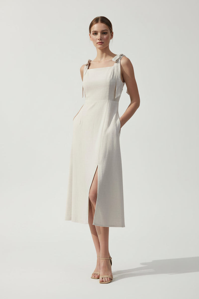 Woman wearing an oatmeal linen blend dress with a slit on a gray background