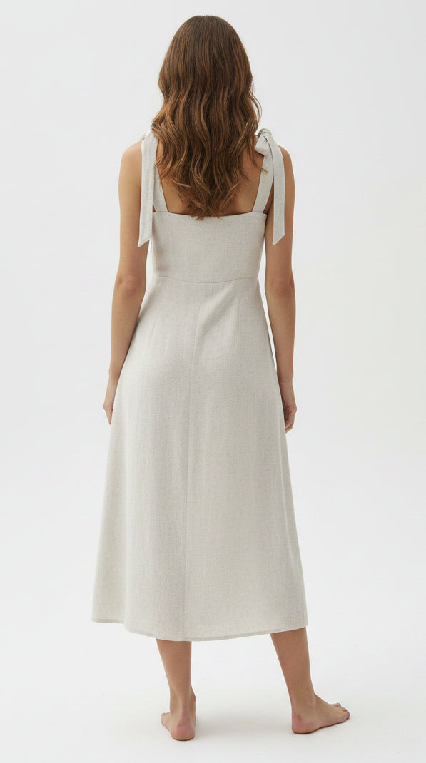 Back view of a woman wearing an oatmeal linen blend dress with a slit on a gray background