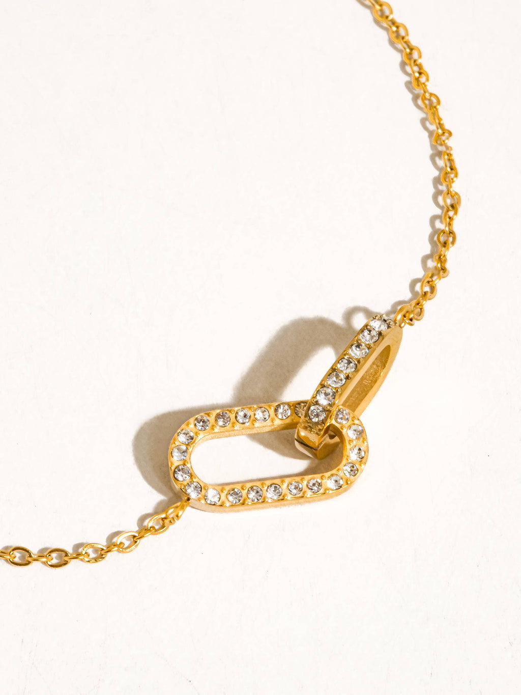 A gold chain necklace featuring double interlocking oval link design pendant paved with CZ stones, displayed on a clean white background.
