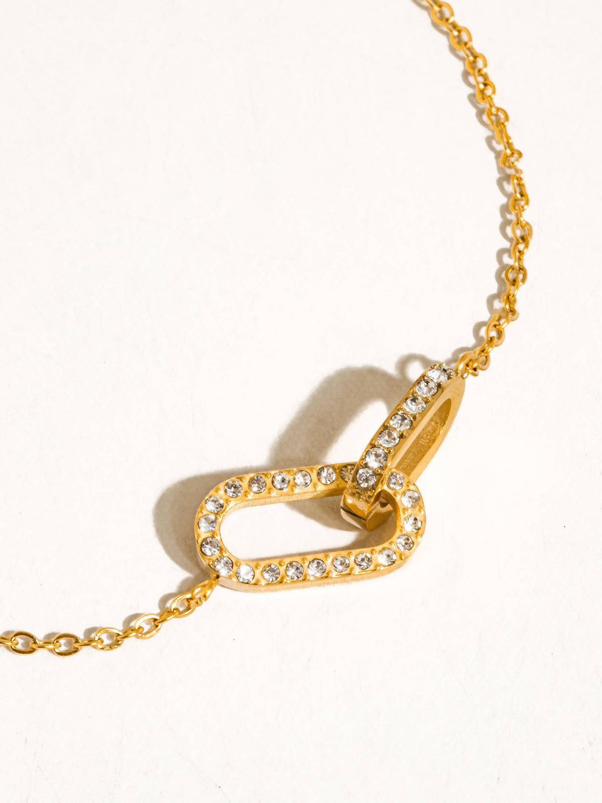A gold chain necklace featuring double interlocking oval link design pendant paved with CZ stones, displayed on a clean white background.