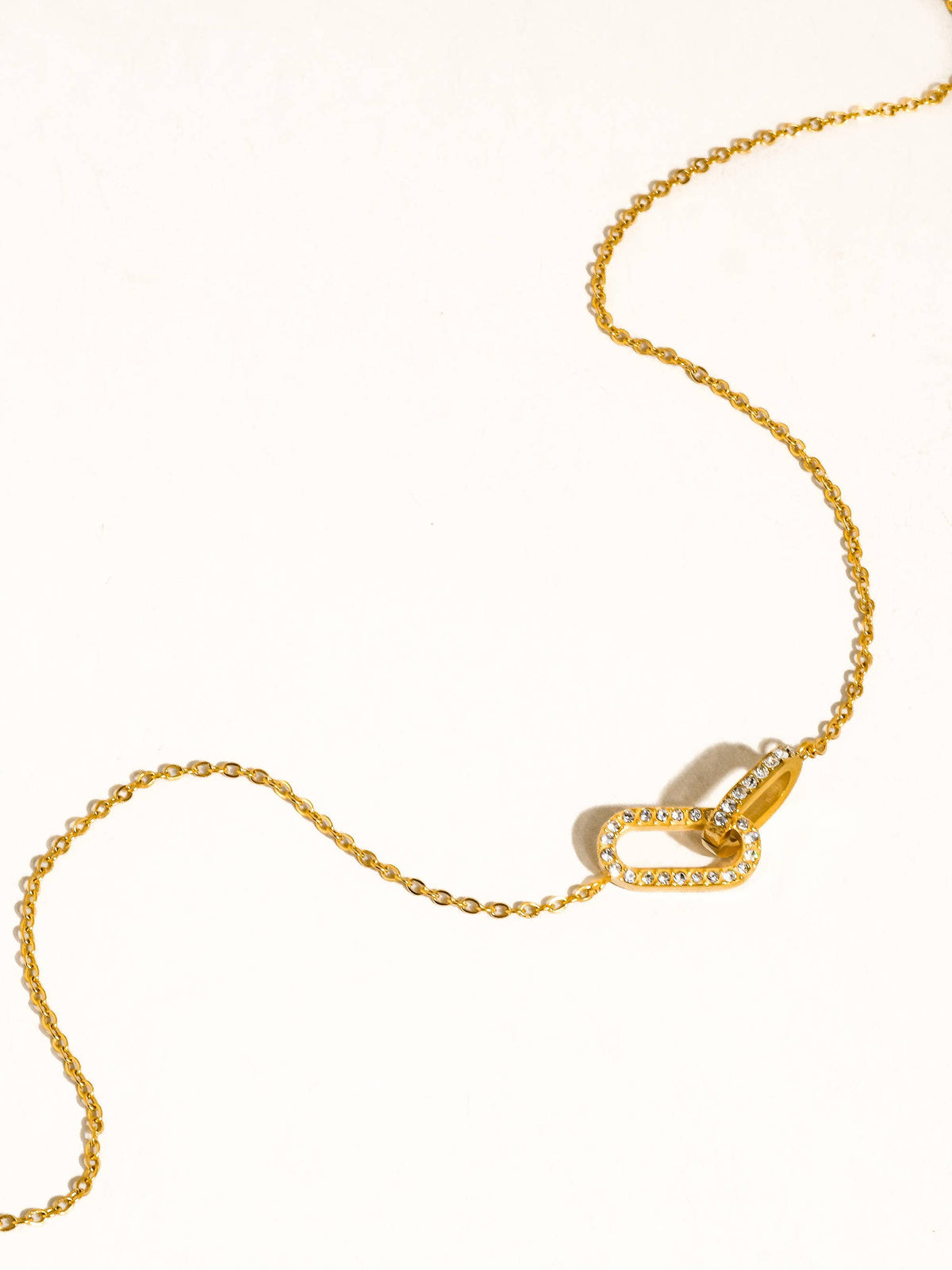 A delicate gold chain necklace featuring a double interlocking oval link design, one of which is paved with CZ stones, displayed on a clean white background.