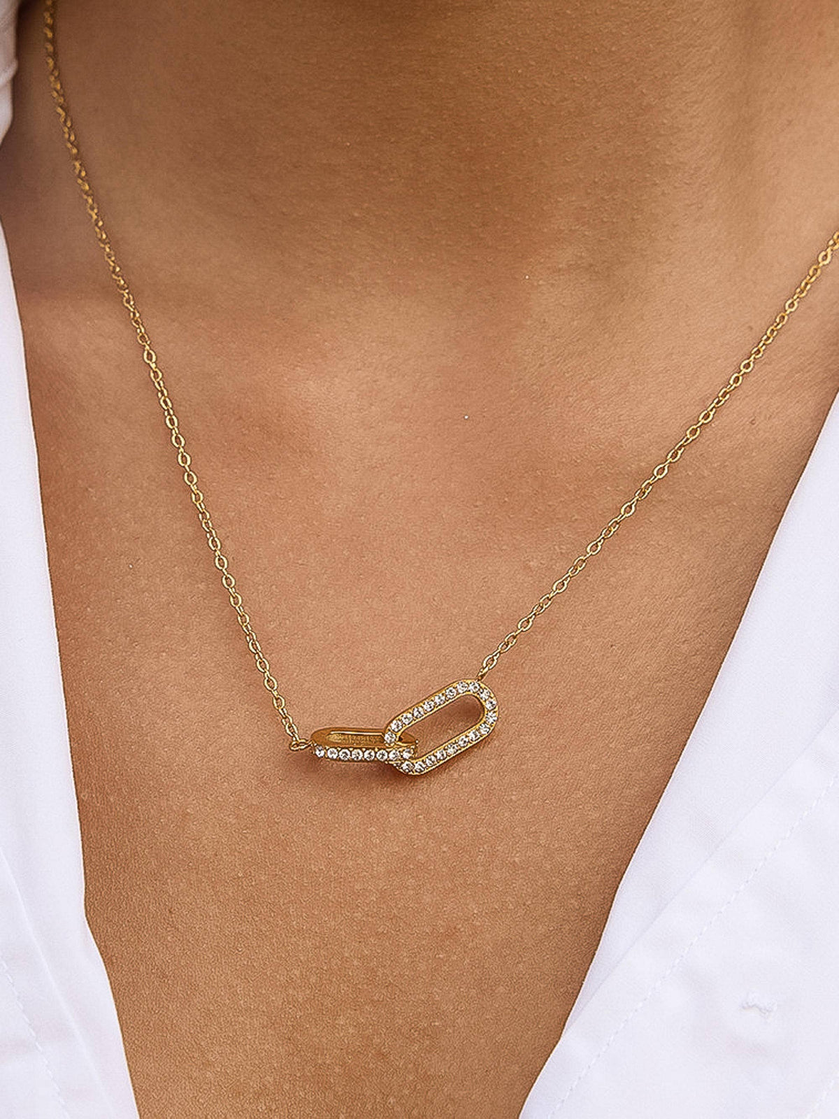 A gold chain necklace featuring double interlocking oval link design pendant paved with CZ stones, displayed on a clean white background.