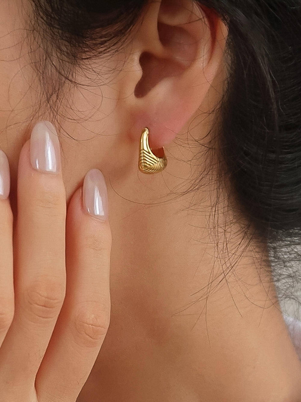 Woman wearing 18k gold-plated textured hoop earrings