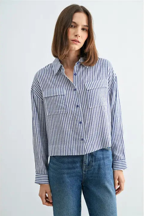 Woman wearing blue and white textured stripe shirt with front pockets and banded with jeans on a grey background