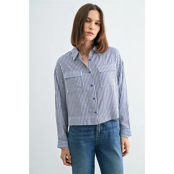 Woman wearing blue and white textured stripe shirt with front pockets and banded with jeans on a grey background