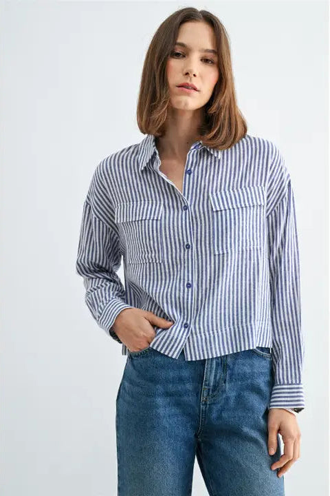 Woman wearing blue and white textured stripe shirt with front pockets and banded with jeans on a grey background
