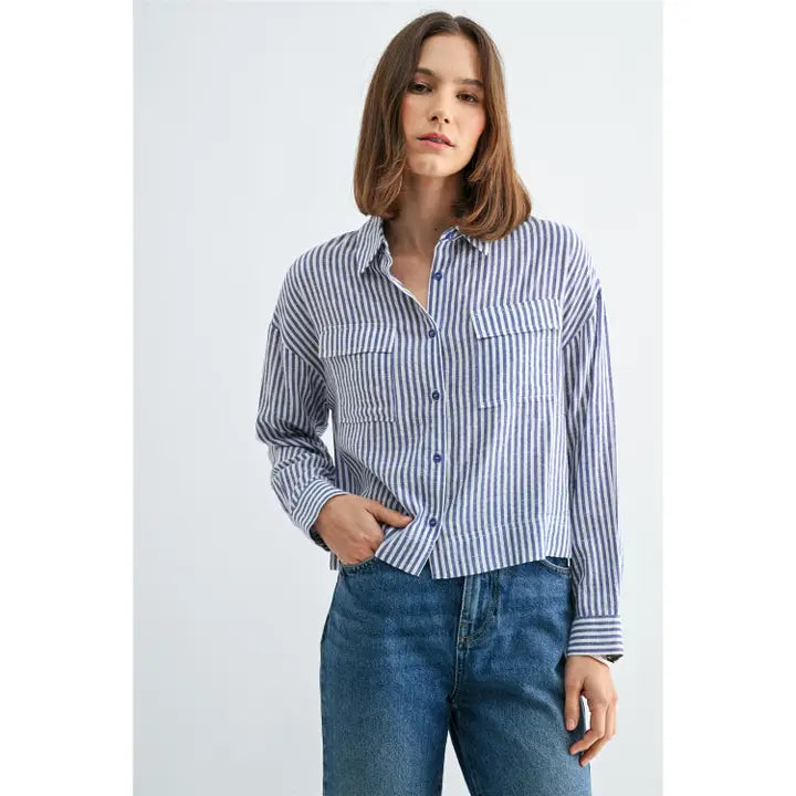 Woman wearing blue and white textured stripe shirt with front pockets and banded with jeans on a grey background