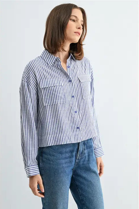 Woman wearing blue and white textured stripe shirt with front pockets and banded with jeans on a grey background
