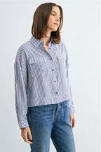 Woman wearing blue and white textured stripe shirt with front pockets and banded with jeans on a grey background