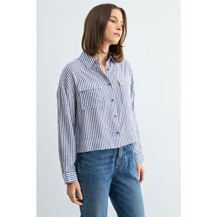 Woman wearing blue and white textured stripe shirt with front pockets and banded with jeans on a grey background