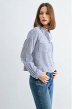 Woman wearing blue and white textured stripe shirt with front pockets and banded with jeans on a grey background
