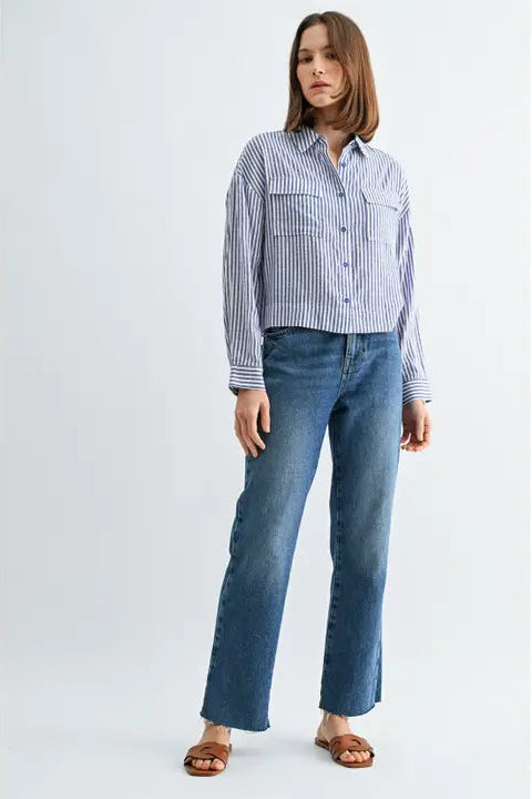 Woman wearing blue and white textured stripe shirt with front pockets and banded with jeans on a grey background