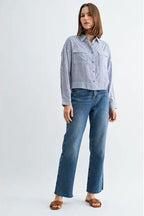 Woman wearing blue and white textured stripe shirt with front pockets and banded with jeans on a grey background