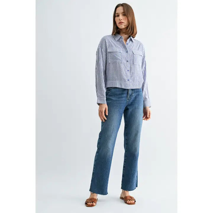 Woman wearing blue and white textured stripe shirt with front pockets and banded with jeans on a grey background