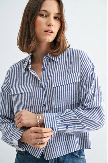Woman wearing blue and white textured stripe shirt with front pockets and banded with jeans on a grey background