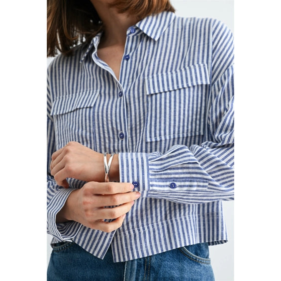 Woman wearing blue and white textured stripe shirt with front pockets and banded with jeans