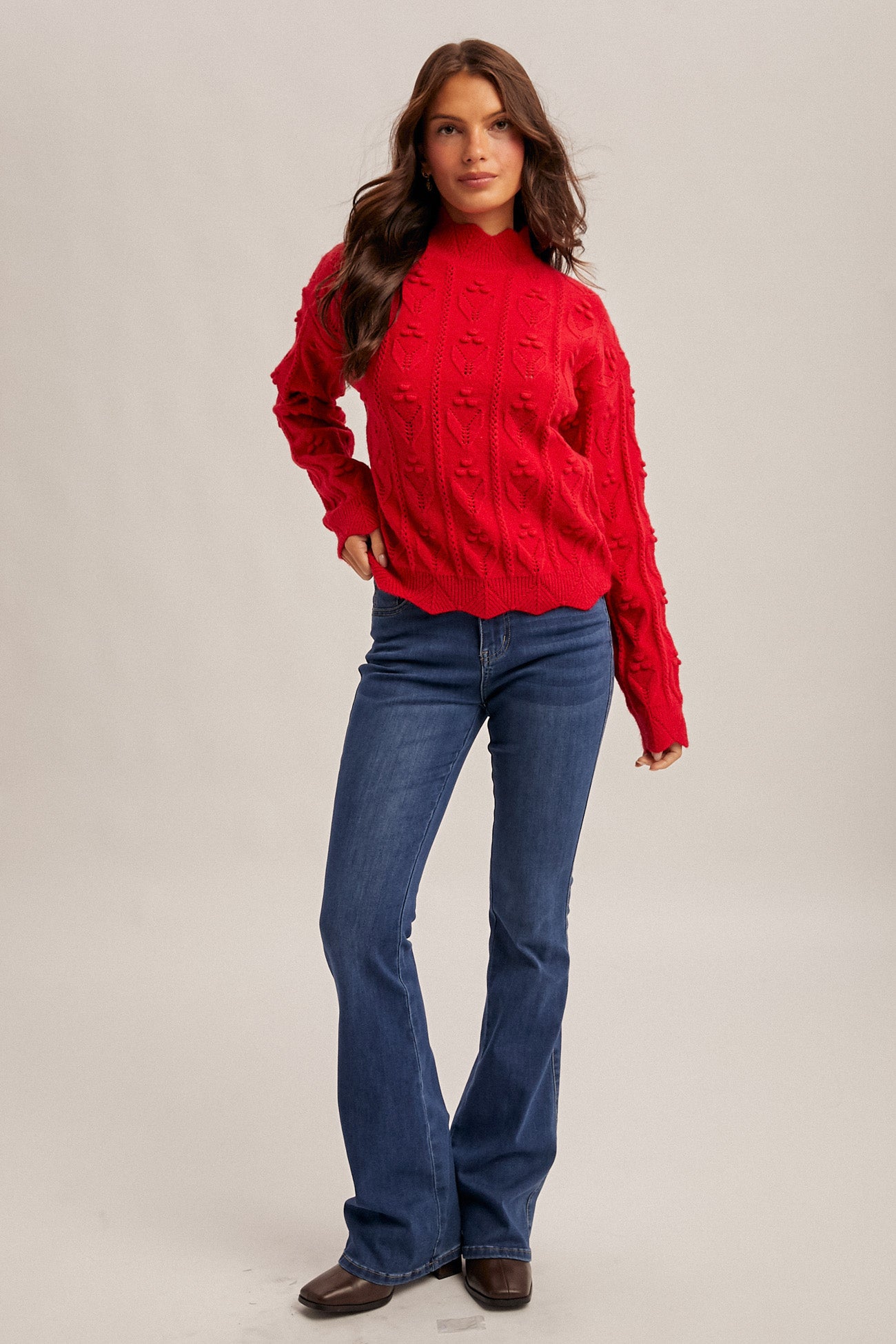 Woman wearing a red crochet knit sweater and blue jeans on a beige background