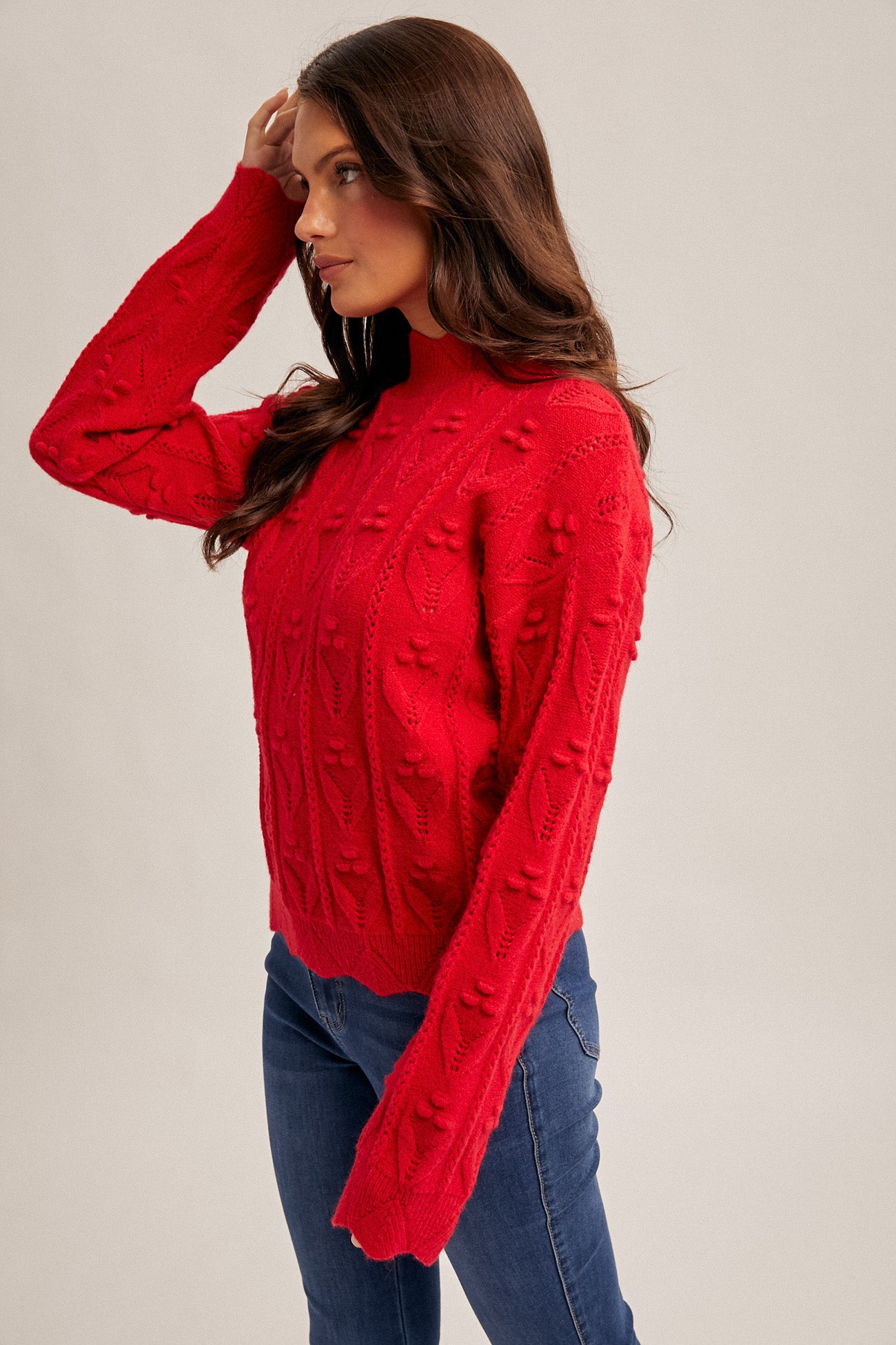 Woman wearing a red crochet knit sweater and blue jeans on a beige background