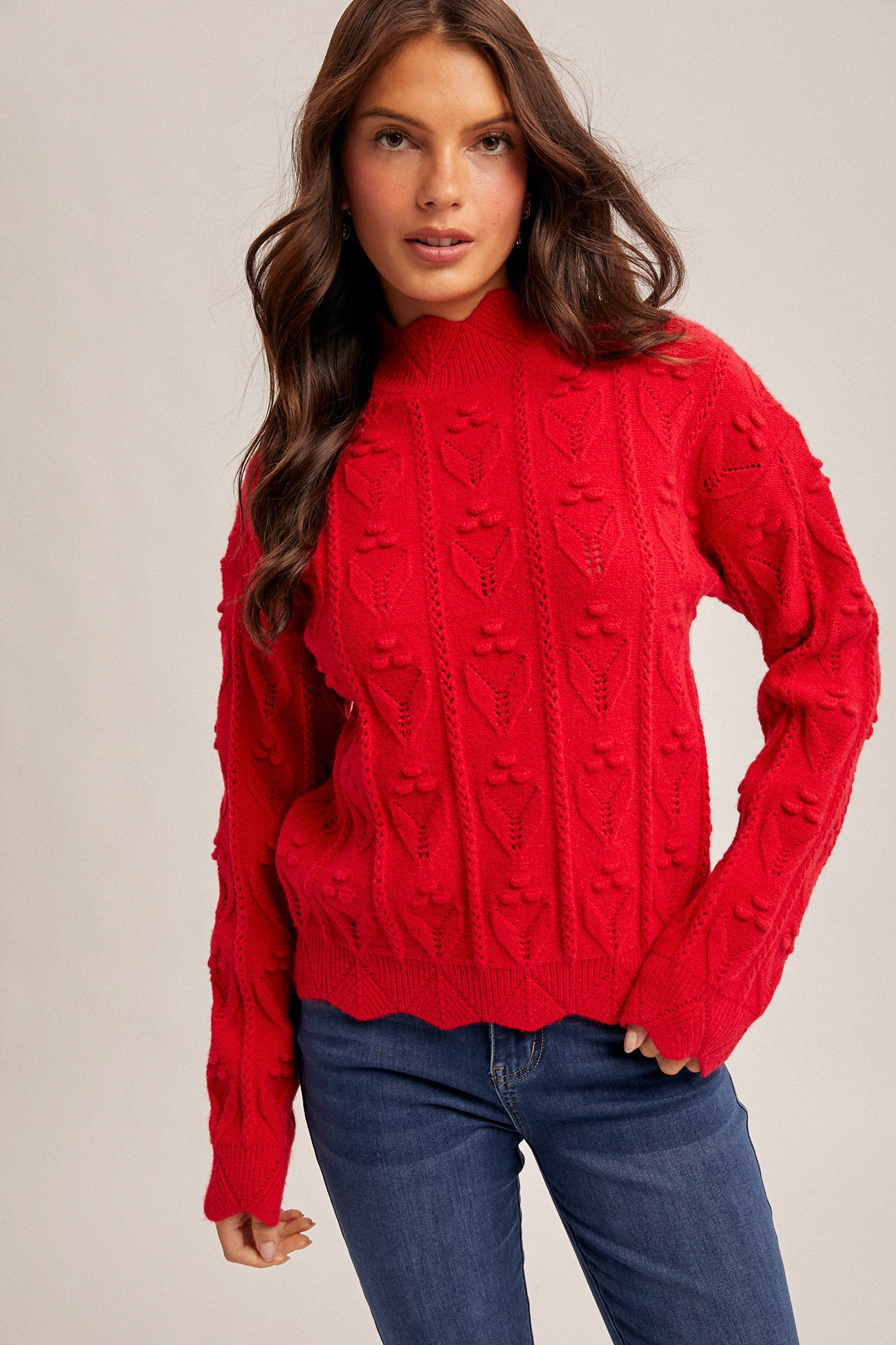 Woman wearing a red crochet knit sweater and blue jeans on a beige background