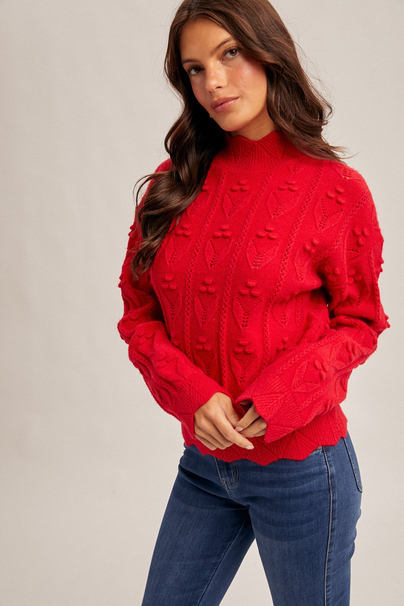 Woman wearing a red crochet knit sweater and blue jeans on a beige background