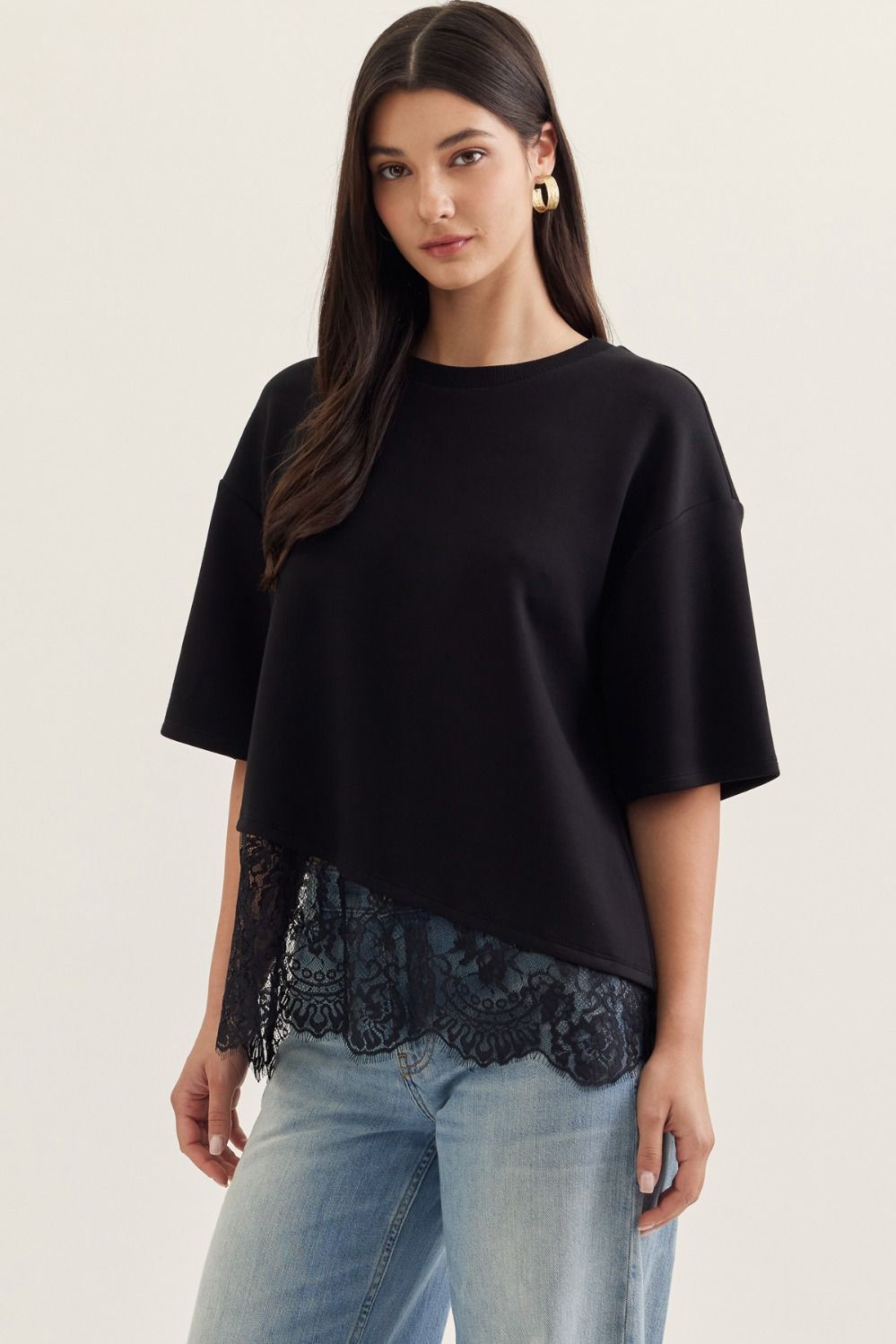 Woman wearing a black top with asymmetrical lace trim and light blue jeans on a plain background