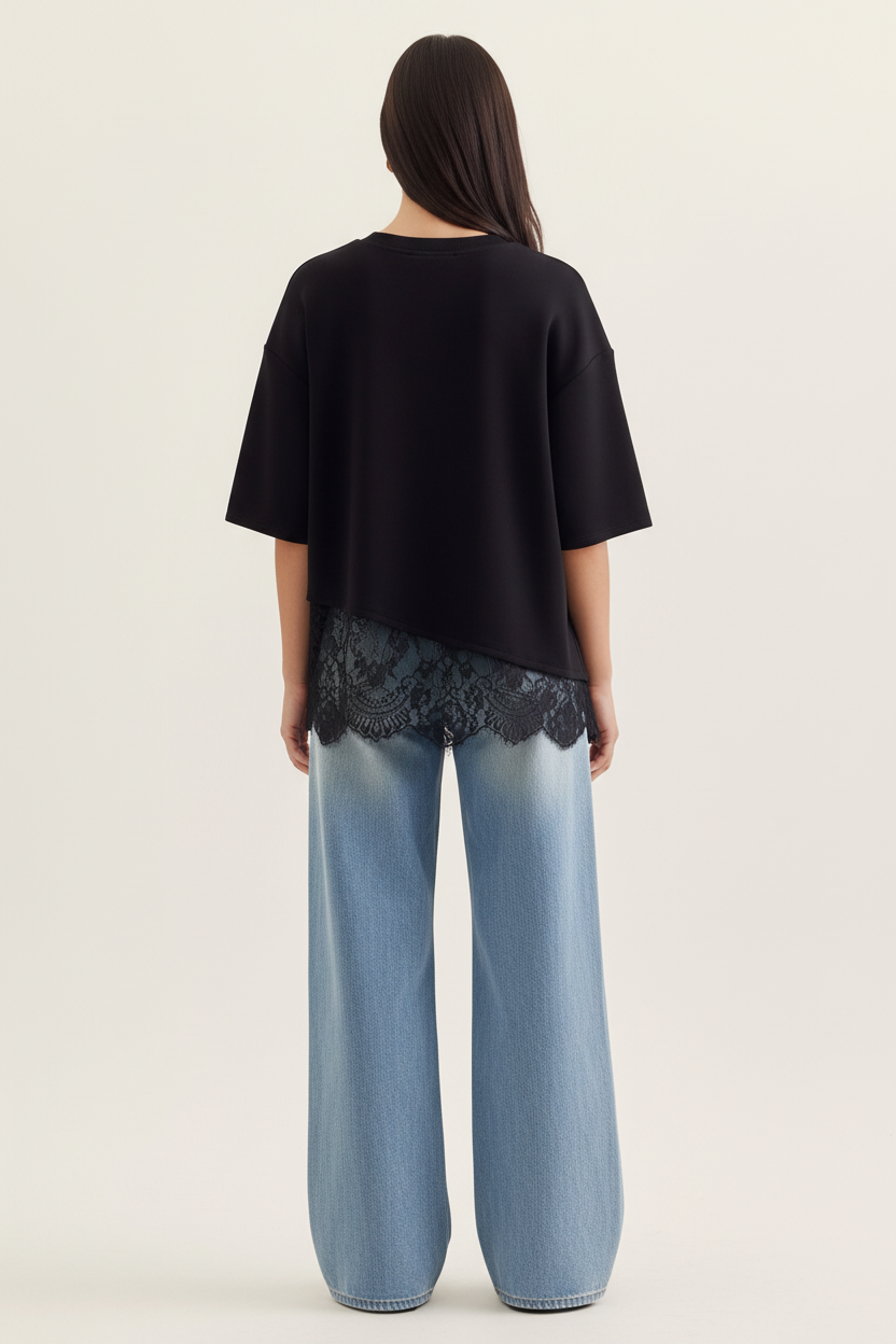 Back view of a woman wearing a black top with asymmetrical lace trim and light blue jeans on a plain background