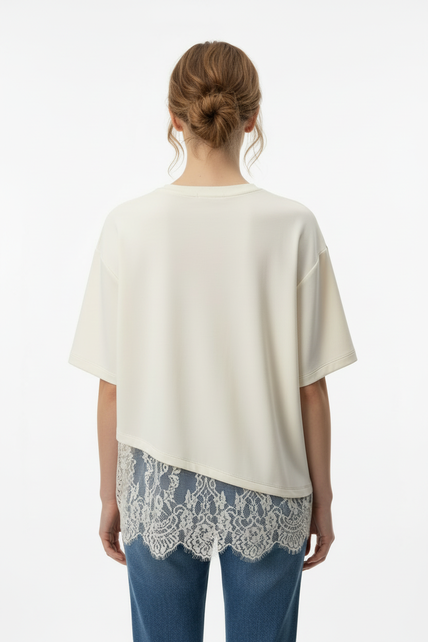 Back view of a woman modeling an ecru knit short-sleeve top with a lace hem detail, paired with light blue jeans, against a plain light gray background.