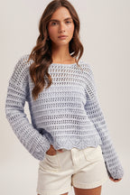 Woman wearing a sky blue crochet top, white shorts and straw hat on a plain background