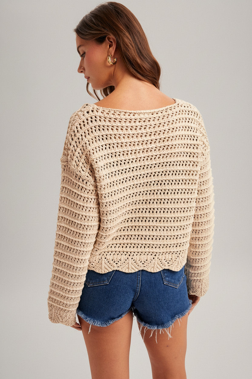 Back view of a woman wearing an ecru crochet long sleeve top and denim shorts on a plain background