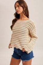 Woman wearing an ecru crochet long sleeve top and denim shorts on a plain background