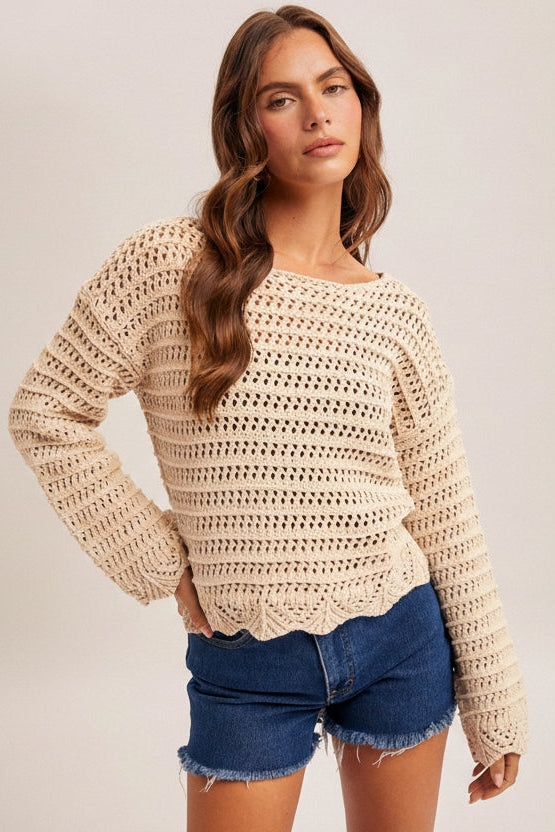 Woman wearing an ecru crochet long sleeve top and denim shorts on a plain background