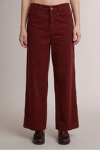 A person wearing high-waisted, wide-leg trousers in a deep burgundy corduroy fabric with a small white polka dot pattern, paired with dark brown leather shoes, against a plain light gray studio background.