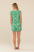 Back view of a woman wearing green and white tropical print top and shorts against a beige background