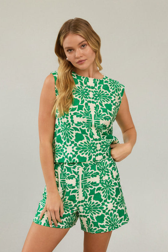 Woman wearing green and white tropical print top and shorts against a beige background