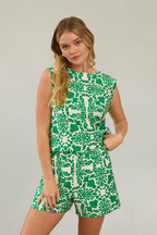 Woman wearing green and white tropical print top and shorts against a beige background