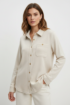 A woman wearing an oatmeal colored button-up shacket against a white background
