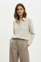 A close-up of a woman wearing an oatmeal colored button-up shacket and tan trousers