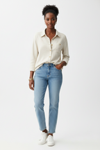 A woman modeling an oatmeal colored  button-up shacket with light-wash blue jeans and white sneakers, standing against a plain white studio background.