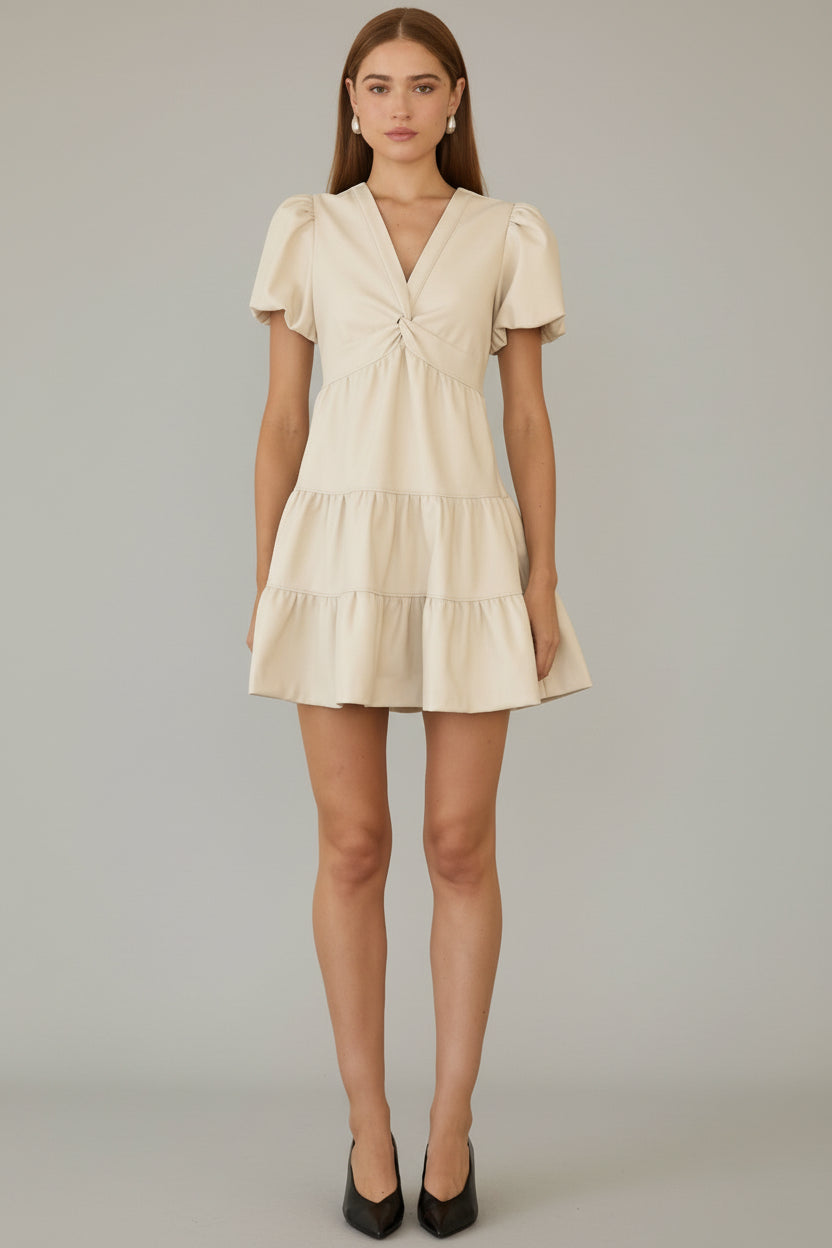 Woman wearing an ivory tiered dress with front twist detail neckline against a gray background