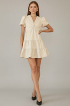 Woman wearing an ivory tiered dress with front twist detail neckline against a gray background