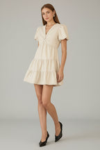 Woman wearing an ivory tiered dress with front twist detail neckline against a gray background