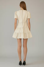 Back view of a woman wearing an ivory tiered dress with front twist detail neckline against a gray background