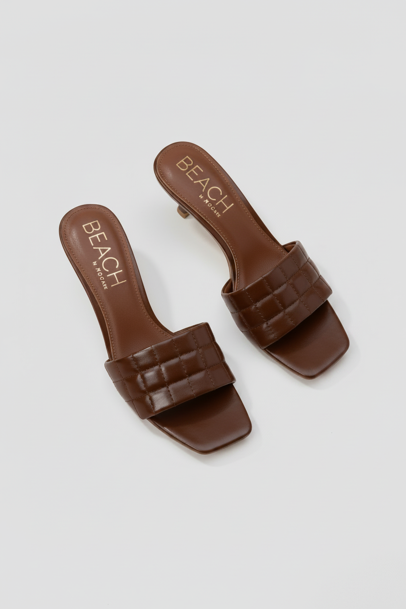 Pair of brown sandals with 'BEACH' branding on a beige background